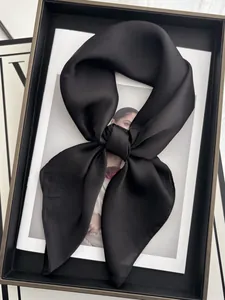 Détail d'un foulard carré en satin de soie noir noué en nœud sur un magazine de mode