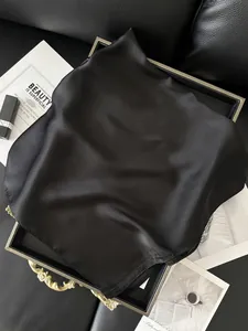 Détail d'un élégant foulard carré en satin noir plié sur un plateau de luxe doré