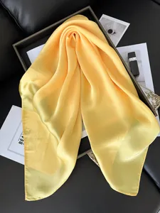 Détail du foulard en satin de soie jaune vif avec texture lisse et drapé élégant