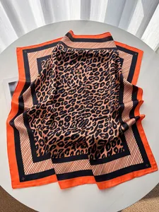 Gros plan du foulard en soie à imprimé léopard avec bordure orange sur table blanche