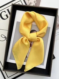 Détail d'un carré de soie jaune gingembre noué en boucle sur un plateau noir élégant