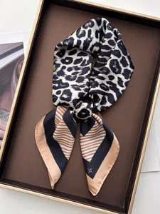 Détail d'un foulard en soie léopard avec bordure rayée orange sur plateau chic