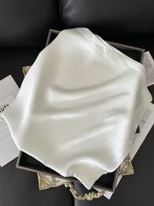 Détail d'un foulard carré en satin blanc brillant posé sur un plateau décoratif doré