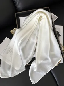 Détail d'un foulard en soie blanc nacré avec texte élégant sur un plateau noir