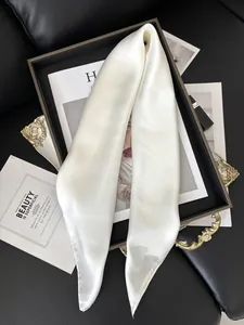 Détail de la texture d'un foulard en soie satinée blanc perle drapé sur un plateau