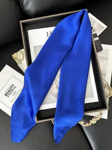 Détail d'un twilly en satin bleu klein enroulé autour de l'anse d'un sac en cuir noir