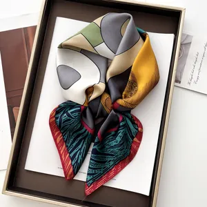 Close-up of elegant silk square scarf with geometric and leaf patterns in a wooden tray