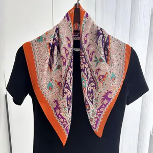 Close-up of paisley print silk scarf with vibrant orange border on black clothing