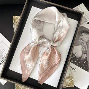 Detail of silk square scarf tied in a bow with elegant floral patterns on leather tray