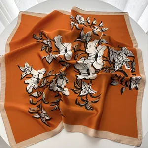 Detail of silk square scarf featuring orange floral prints draped on a white table