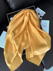 Détail d'un foulard en satin de soie dorée avec reflet métallique et bordures cousues