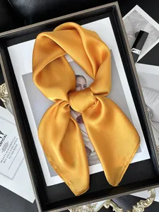 Gros plan d'un foulard en satin de soie jaune gingembre noué en un nœud élégant sur fond noir