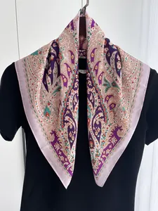Detail of light pink silk-like square scarf with intricate paisley patterns on black fabric