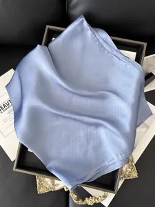 Vue rapprochée du foulard carré en satin bleu clair avec texture soyeuse sur plateau doré