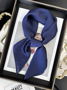 Détail du foulard en satin bleu foncé noué en nœud sur fond de magazine de luxe