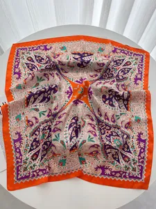 Detailed view of orange and purple paisley silk scarf texture on a white surface