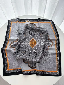 Detail view of a 70cm silk scarf featuring grey paisley patterns and vibrant orange borders