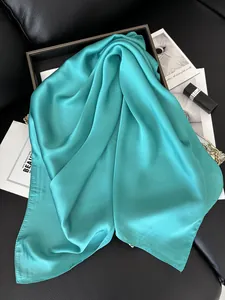 Gros plan d'un foulard carré en satin bleu sarcelle brillant avec une texture lisse