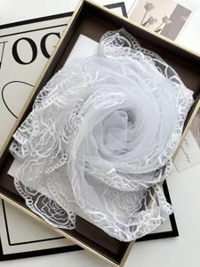 Detail of white bridal lace shawl with camellia embroidery in a gold gift box