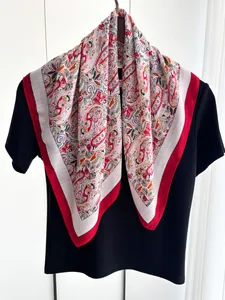 Detailed view of paisley pattern silk scarf with red border draped on a black shirt