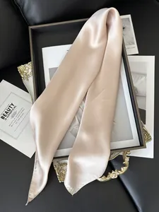 Détail d'un élégant foulard Twilly en satin champagne sur une texture cuir noir chic