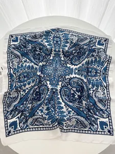 Detail of square silk scarf featuring blue paisley patterns on a white table