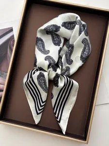 Detailed close-up of a luxury paisley silk scarf with black borders on a display tray