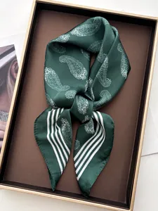 Detail of silk scarf showing green paisley pattern and smooth texture in gift box