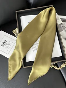 Détail de la texture d'une écharpe en satin doré olive sur un plateau de luxe chic