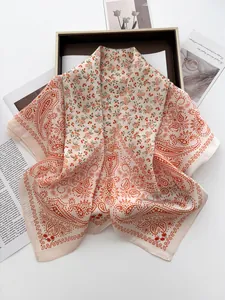 Detail of silk-texture square scarf with orange floral and paisley patterns on a tray