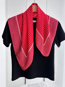 Detail of red polka dot silk scarf tied over a black shirt showing elegant draped texture