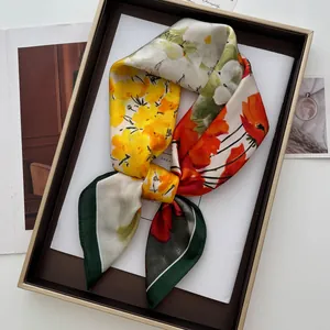 Detail of floral printed satin scarf with yellow flowers and dark green border in tray