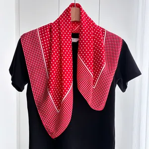 Close-up of a red square silk scarf with white polka dots on a display stand