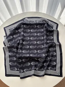 Detailed flat lay of navy blue paisley silk scarf with striped border on a white table