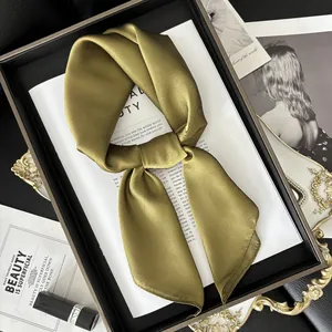 Foulard en satin de soie vert olive brillant noué élégamment sur un plateau doré