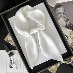 Élégant foulard en soie satinée blanche plié sur un plateau avec accessoires de luxe