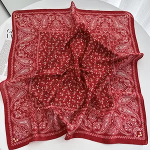 Close-up of a red square silk scarf with paisley patterns and floral prints on a table