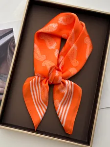 Detailed view of luxury orange silk scarf with paisley and stripe pattern in a gift tray