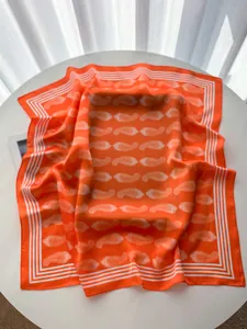 Detailed view of orange paisley silk scarf with striped borders on a white table