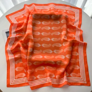 Detailed view of bright orange silk scarf featuring white paisley patterns and striped edges