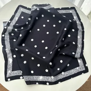 Detail of a black square silk scarf featuring classic white polka dots on a table