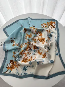 Détail de la texture lisse d'un foulard carré en soie avec des motifs floraux oranges