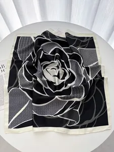 Detailed view of square silk scarf with black and white rose pattern on a white table