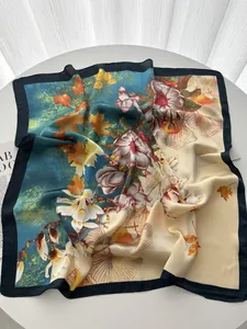 Détail d'un grand carré de soie avec imprimés floral et feuilles d'érable sur table blanche