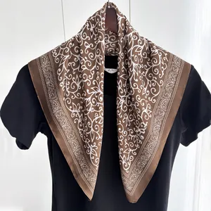 Brown silk-like square scarf with white paisley patterns hanging on a wooden hanger