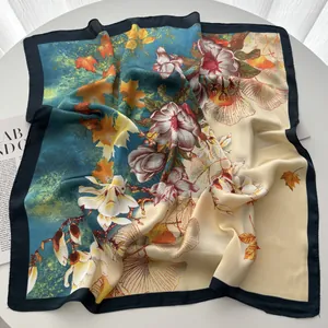 Gros plan d'un foulard carré en soie avec motifs de fleurs, érables et bordure bleue