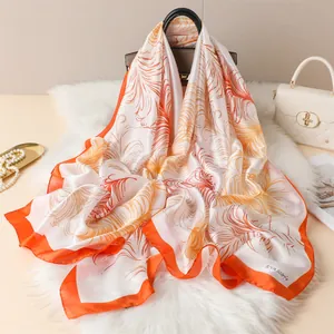 Detail of luxury silk scarf with orange feather patterns draped over a brown handbag