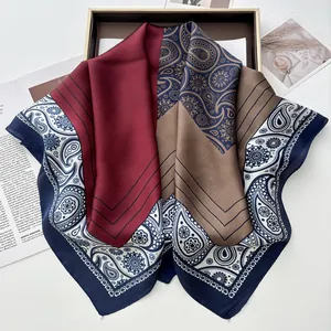 Detail view of paisley print silk scarf in burgundy and brown inside a gold-rimmed gift box