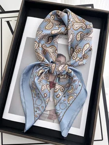 Détail d'un foulard en soie paisley bleu clair noué en nœud sur un plateau luxe