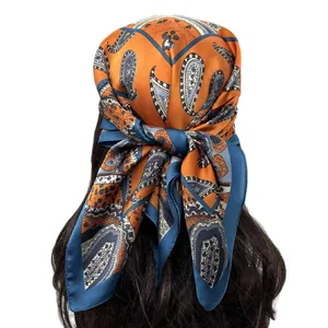 Détail d'un foulard en soie au motif cachemire orange et bleu porté en turban élégant